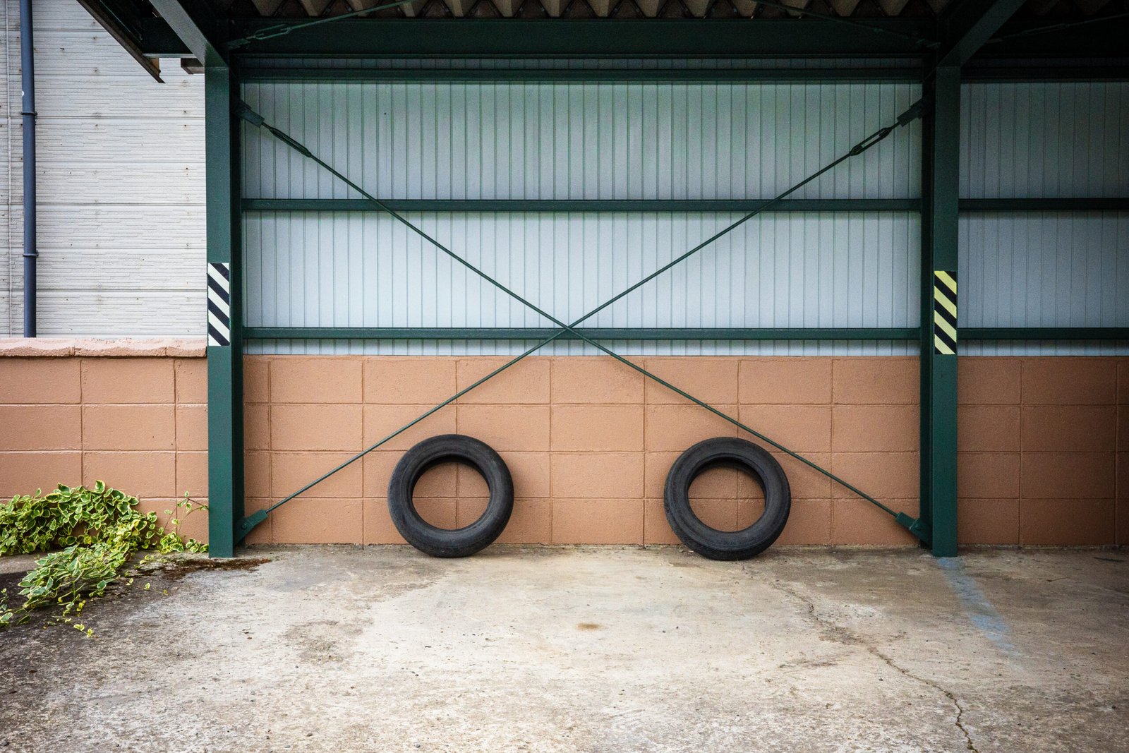 A view of a car port, which backs against a cinder block wall, with two tires leaning against the wall to prevent a car from backing into the wall.