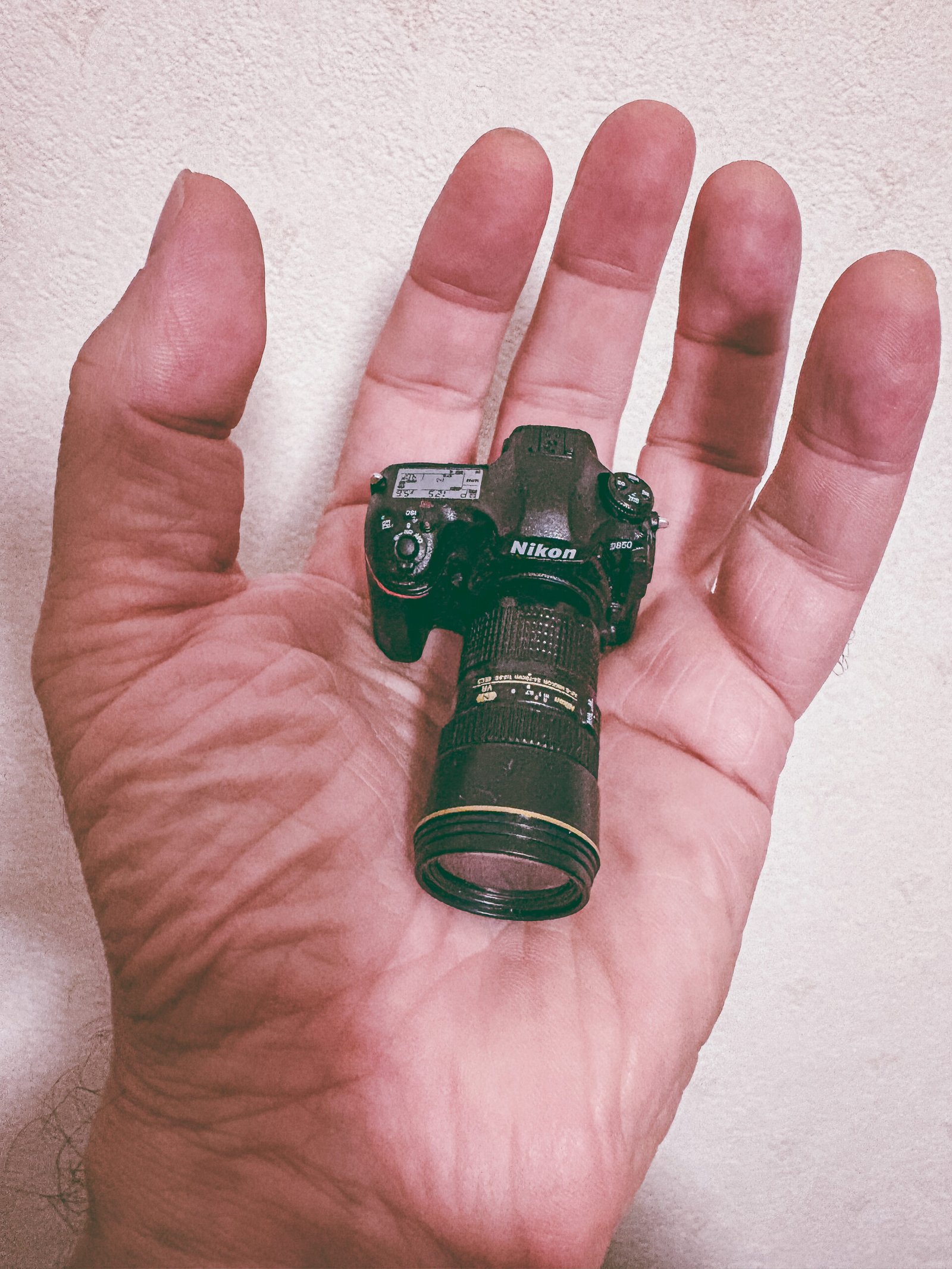 A miniature Nikon camera held in the palm of a man's hand.