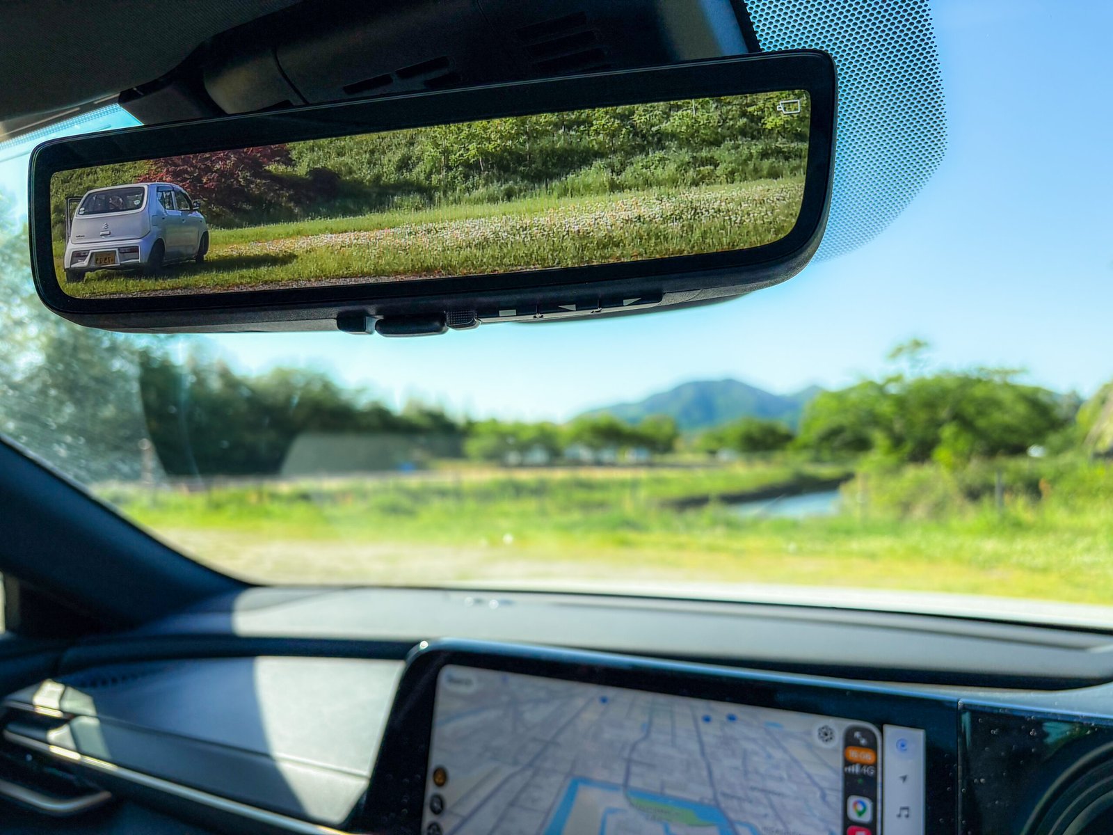 A view from inside a car showing the image of a parked car in the rear view mirror and a blurred images of a landscape outside the front windshield and the car's navigation map.